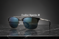 A pair of stylish Xperio Polarised sunglasses with πολωτικοί φακοί rests on polished black marble, while the brand name and logo appear above them against a dark gradient background.